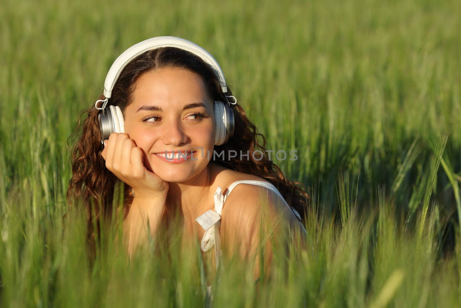 Happy woman listening to music in a green field looking at side