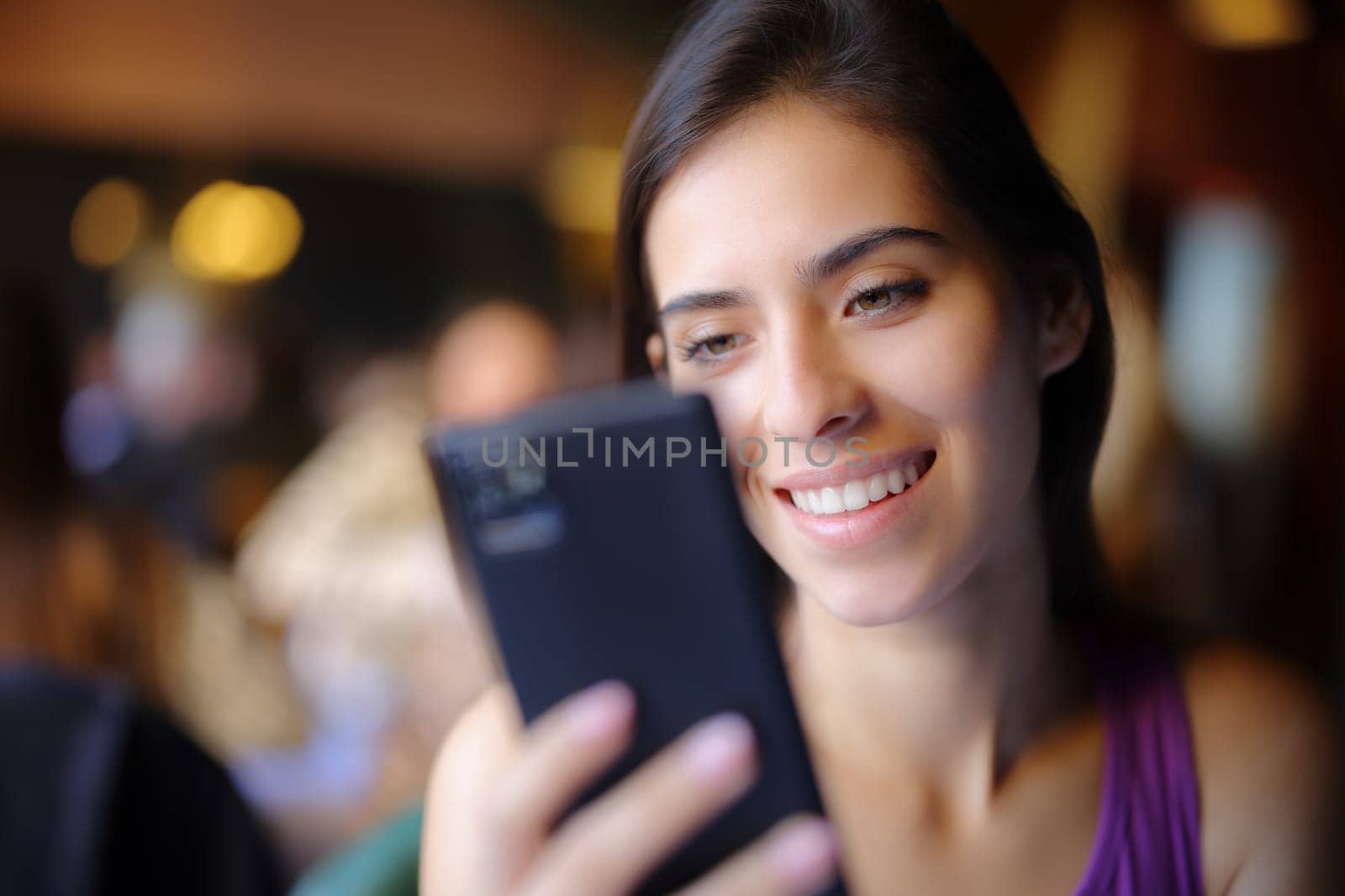 Happy woman in a restaurant using smart phone and smiling
