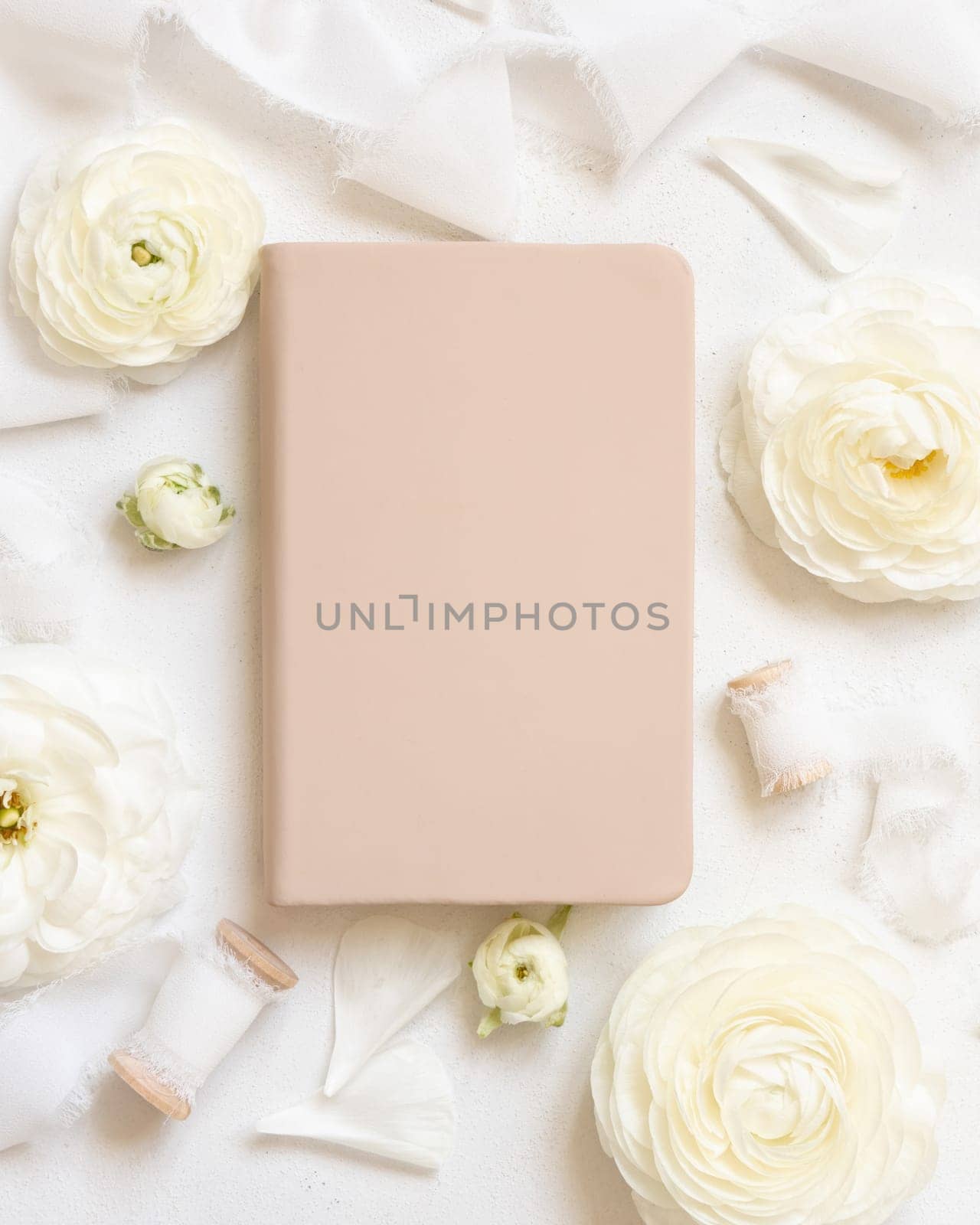 Cream hardcover textbook near cream roses and white silk ribbons top view, mockup. Romantic scene with notebook and pastel flowers. Valentines, Spring or Mothers day concept