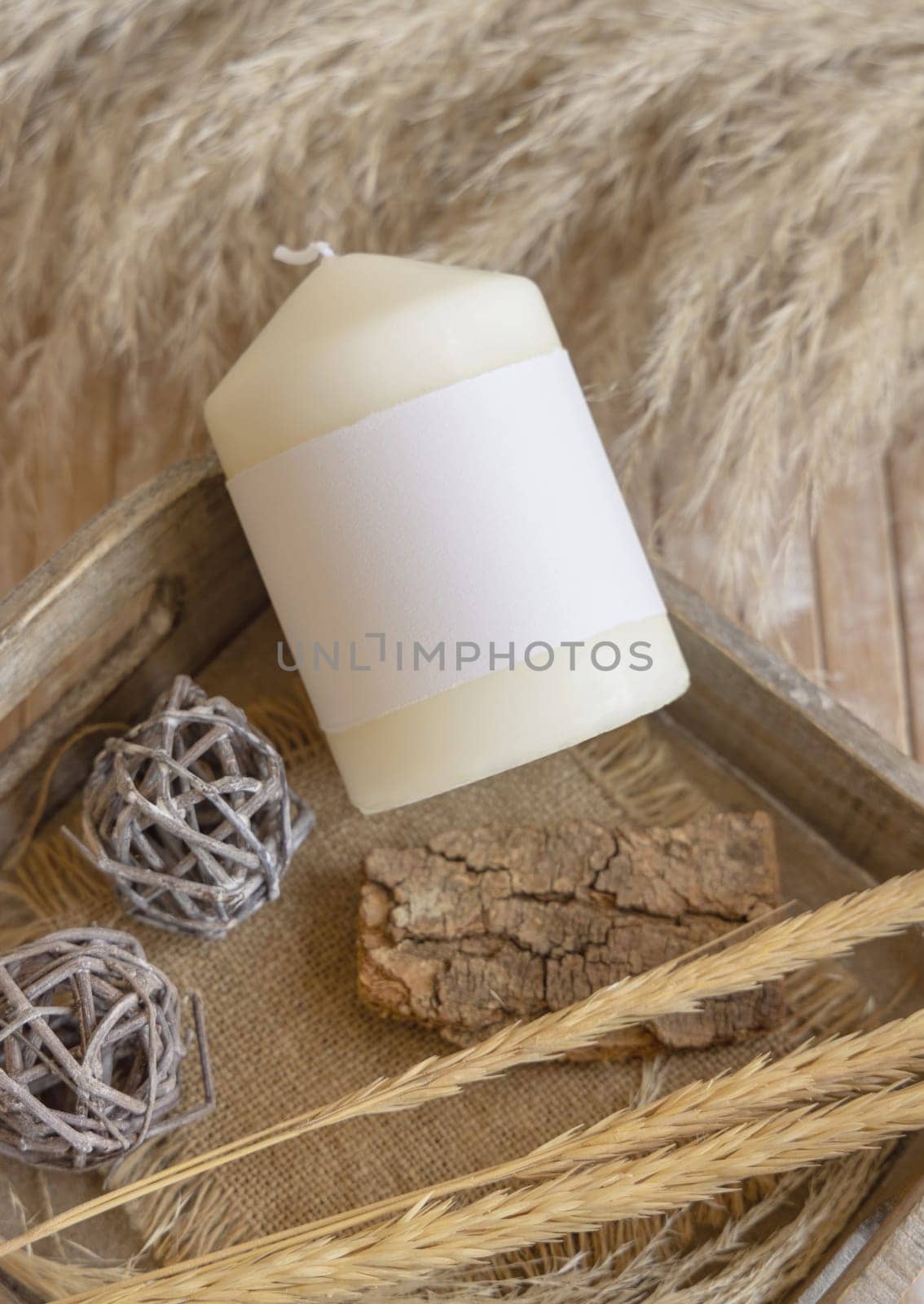 Candle with blank paper label on wooden tray near dried pampas grass and natural decor, Close up, copy space. Boho packaging mock up. Home decorations, Bohemian or scandinavian style