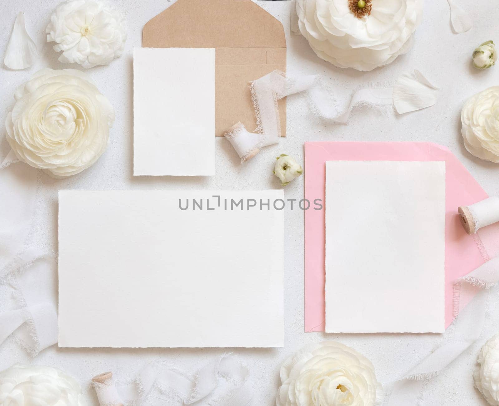 Blank cards and envelopes near cream roses and white silk ribbons top view, mockup. Romantic scene with wedding set and pastel flowers flat lay. Valentines, Spring or Mothers day concept