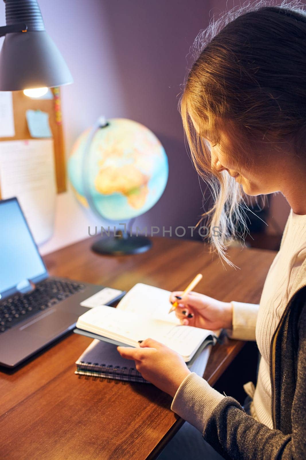 Student learning remotely from home. Young woman having classes online, making notes, reading and learning sitting at desk at home during quarantine