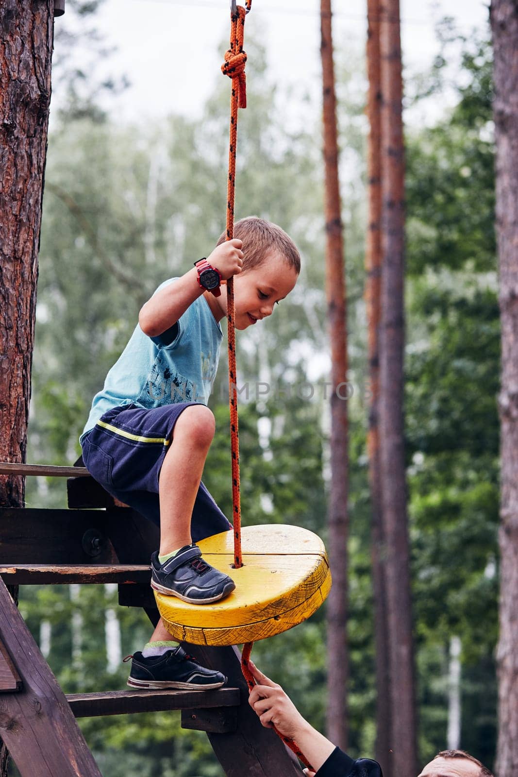 Happy boy getting in the zip line in rope park in forest while spending summer vacation. Real people, authentic situations