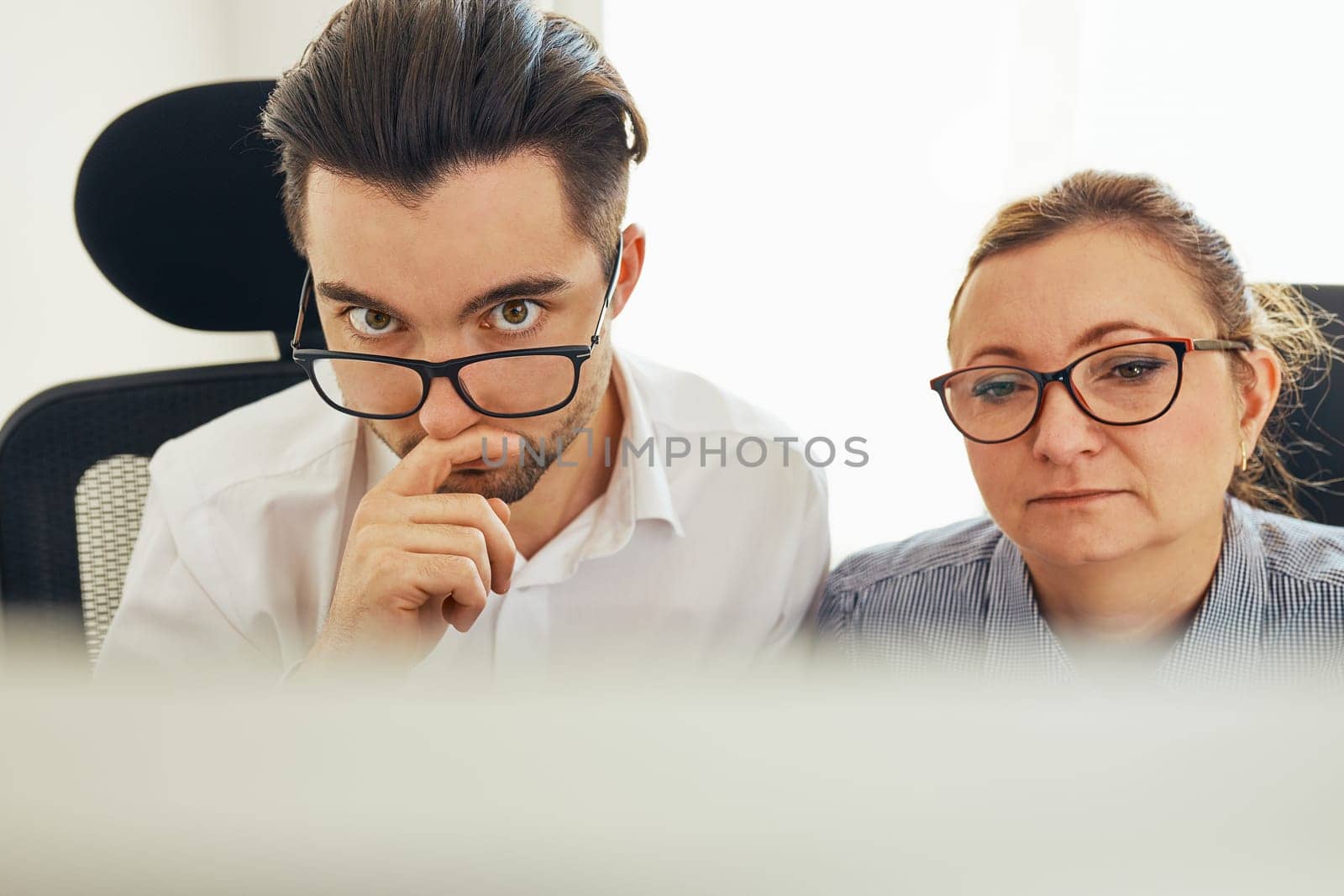 Two business people discussing financial data looking at computer screen. Entrepreneurs working hard sitting at computere screen in office. People having deadline working together. Workmates talking about project