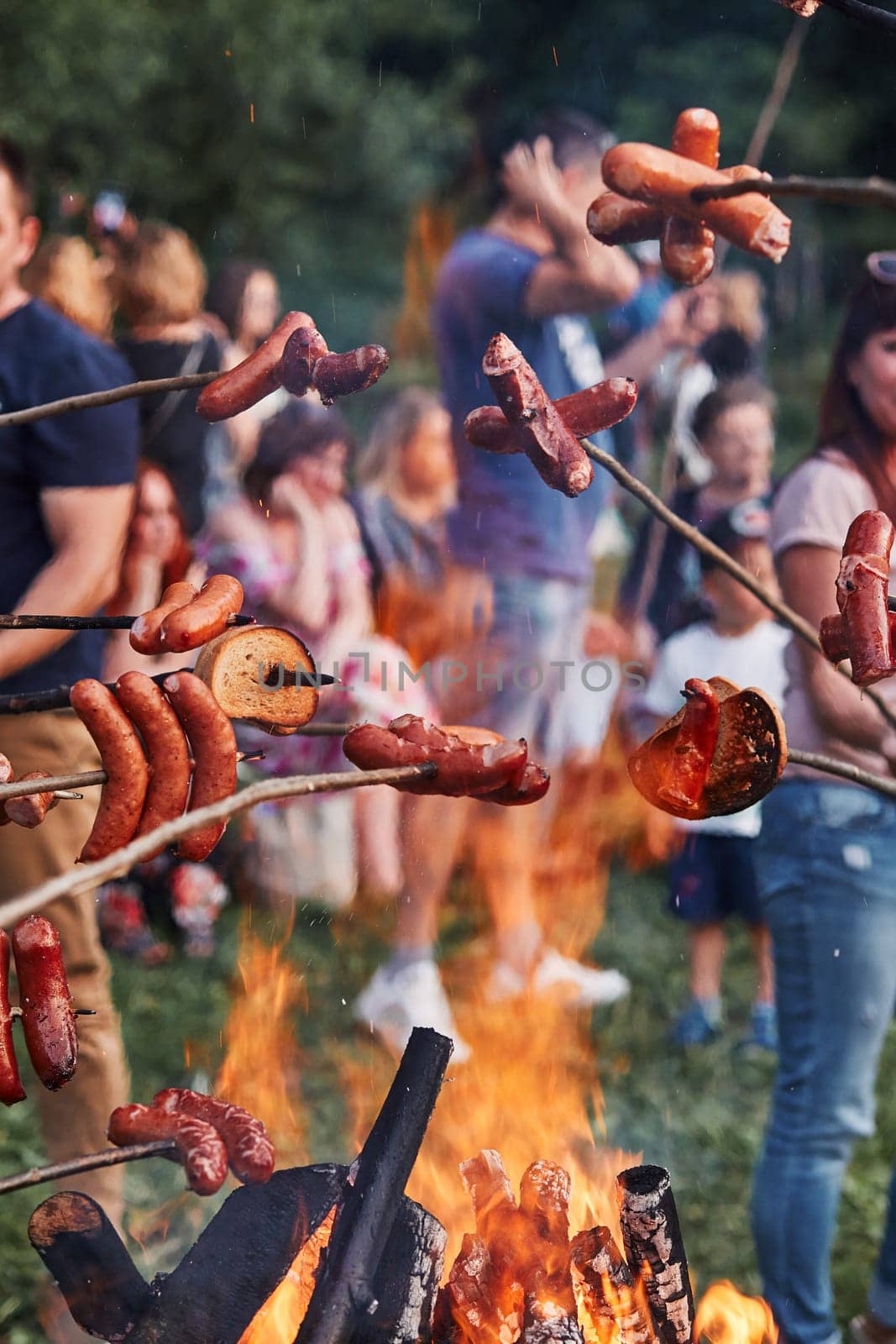 People roasting sausages and bread over a bonfire during picnic party on summer vacation day. Real people, authentic situations