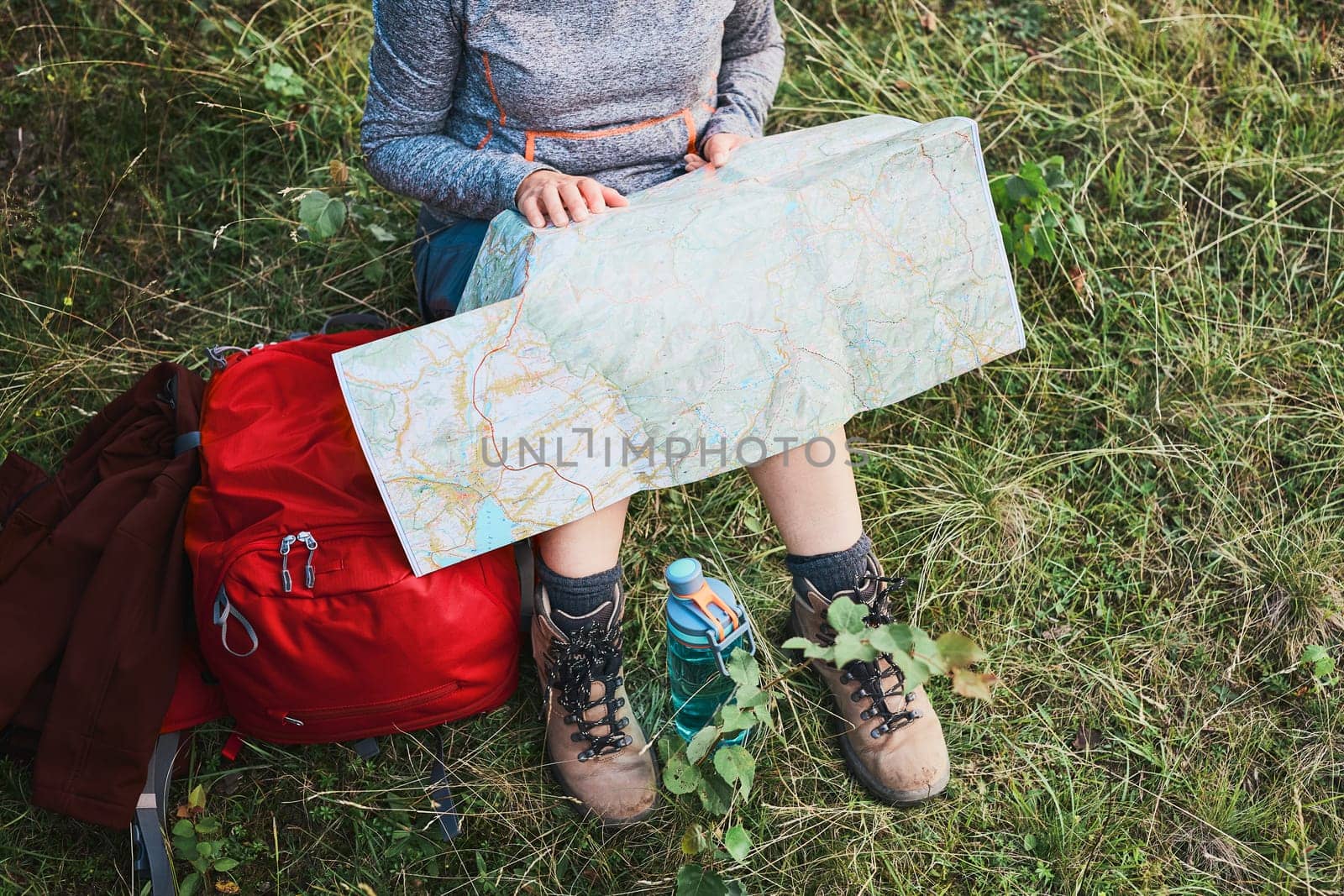 Woman with backpack having break during trip in mountains looking at map sitting on grass on summer vacation day