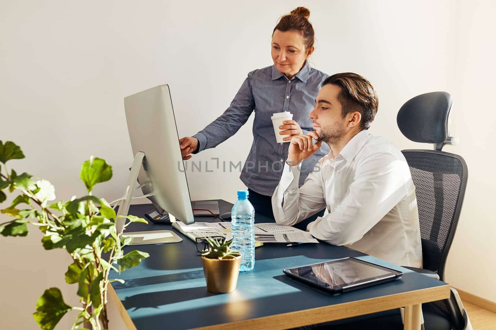 Two business people discussing financial data on computer. Businesswoman working with male colleague in office. People entrepreneurs working with charts and tables on screen. Two people working together. Workmates talking about project