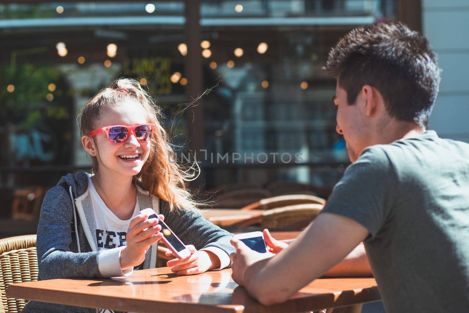 Young woman and man sitting in pavement cafe a the table talking and using mobile phones