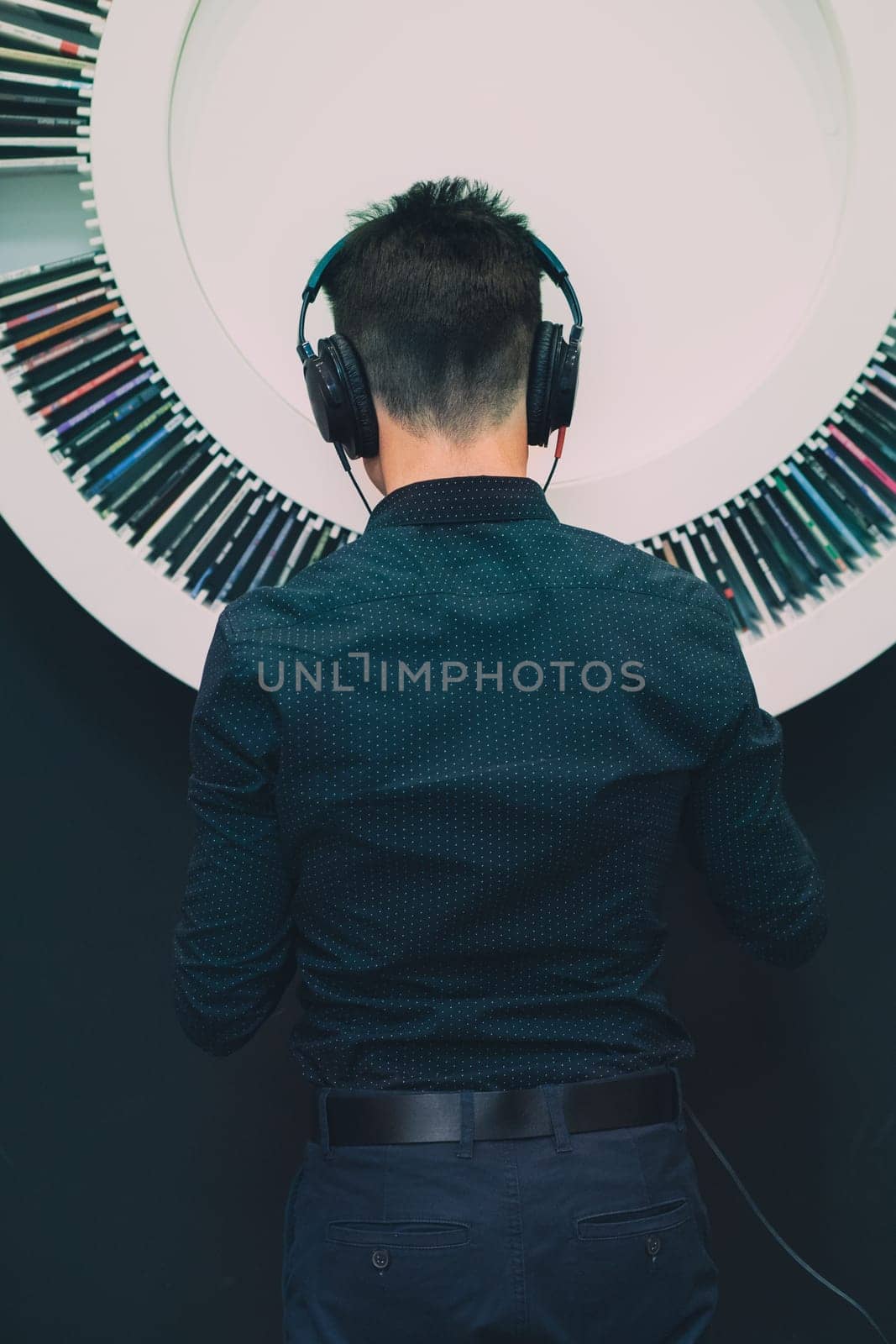 Young man listening to music through headphones standing next to bookshelf with recordings