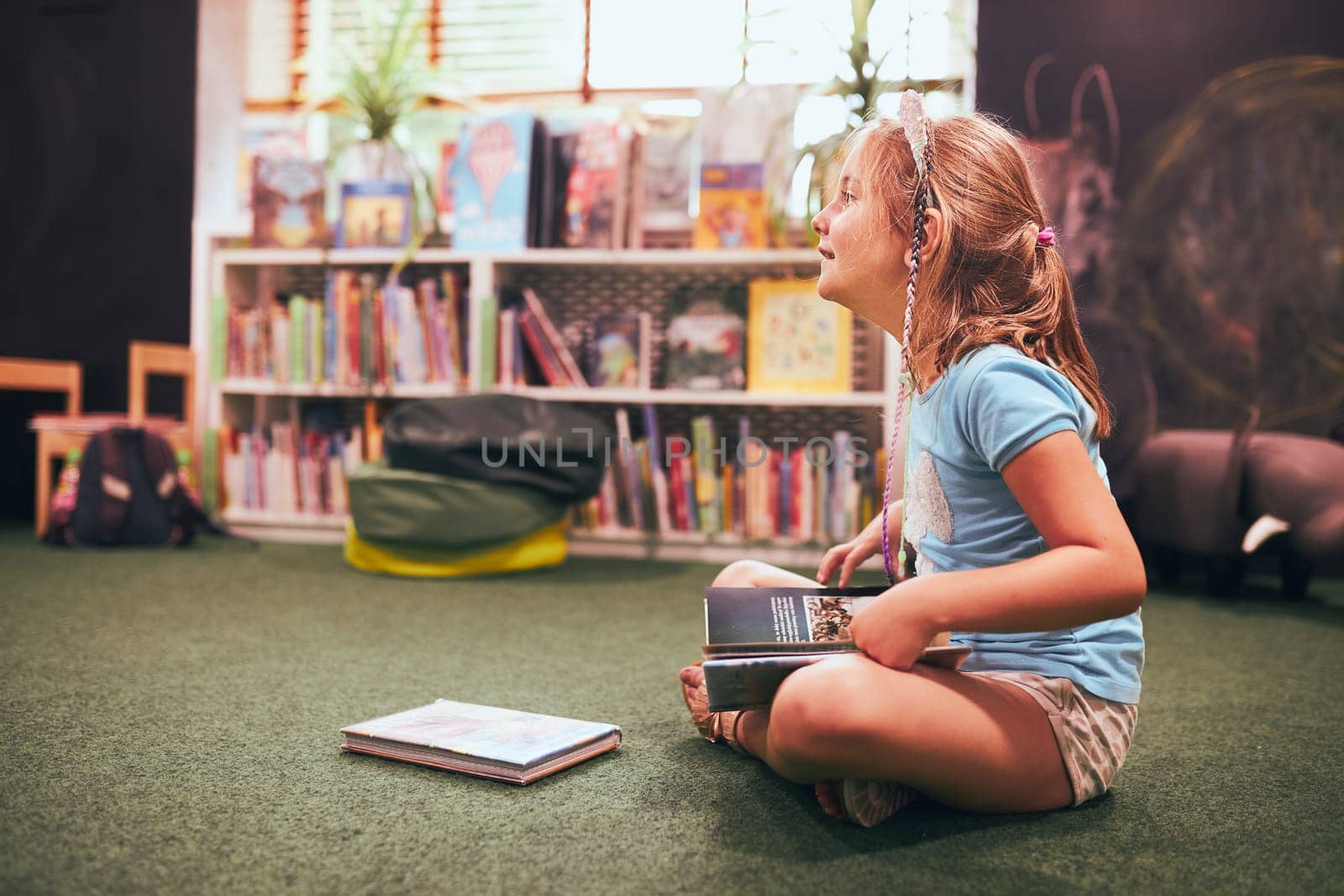 Primary schoolgirl doing homework in school library. Student learning from books. Pupil having fun studying interesting books. Back to school