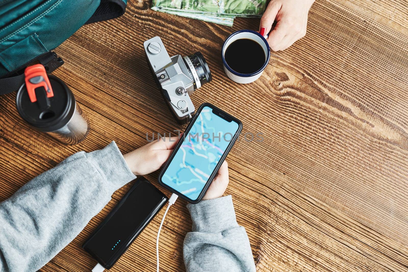 Family planning vacation trip. Girl searching travel destination and routes using navigation map on mobile phone. Charging smartphone with power bank. Using technology while travelling. People sitting at wooden table with camera and backpack during journey. Travel plan concept