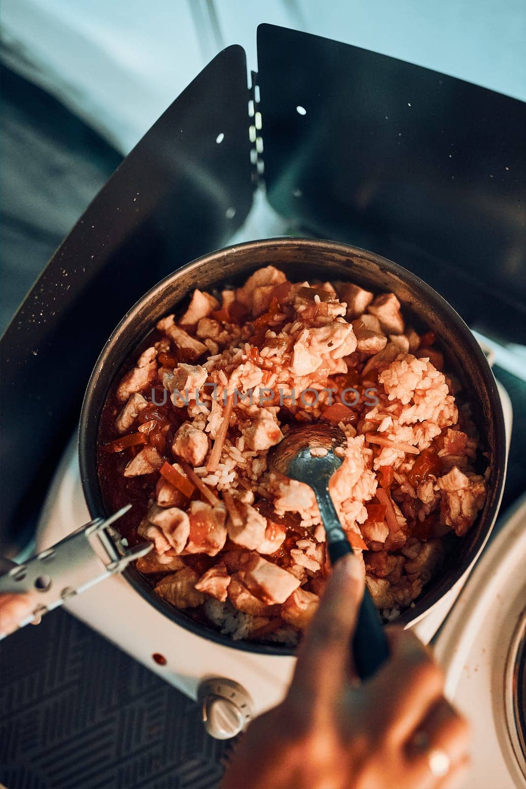 Close up of female hands putting dish with tomato sauce. Woman cooking meal on electric stove on camping during summer vacations. Camping life, preparing a meal