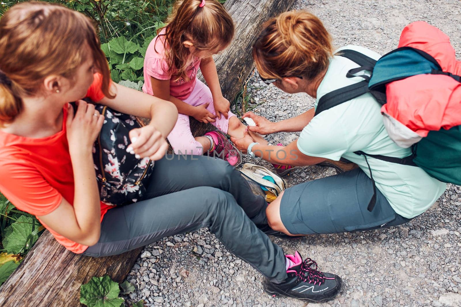 Mother dressing the wound on her little daughter's knee with medicine in spray. Accident happened during family summer vacation trip. People actively spending time