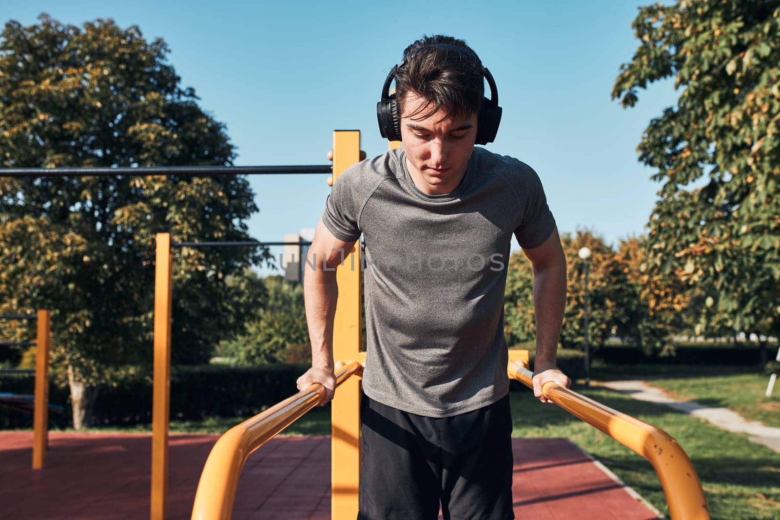 Young man doing dips on parallel bars during his workout in a modern calisthenics street workout park. Man listening to music wearing headphones and sportswear