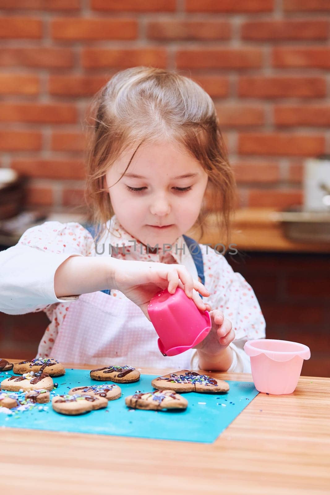 Little girl decorating her baked cookies with colorful sprinkle and icing sugar. Kid taking part in baking workshop. Baking classes for children,  aspiring little chefs. Learning to cook. Combining and stirring prepared ingredients. Real people, authentic situations