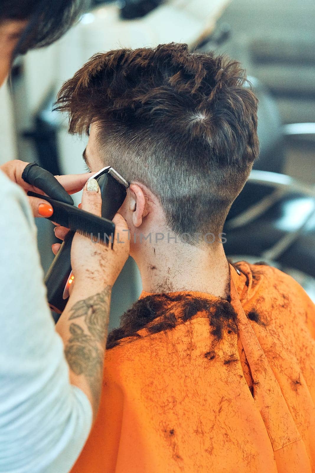 Hairdresser haircutting styling young man's hair in barbershop. Young woman working as a hairdresser in hair salon. Real people, authentic situations