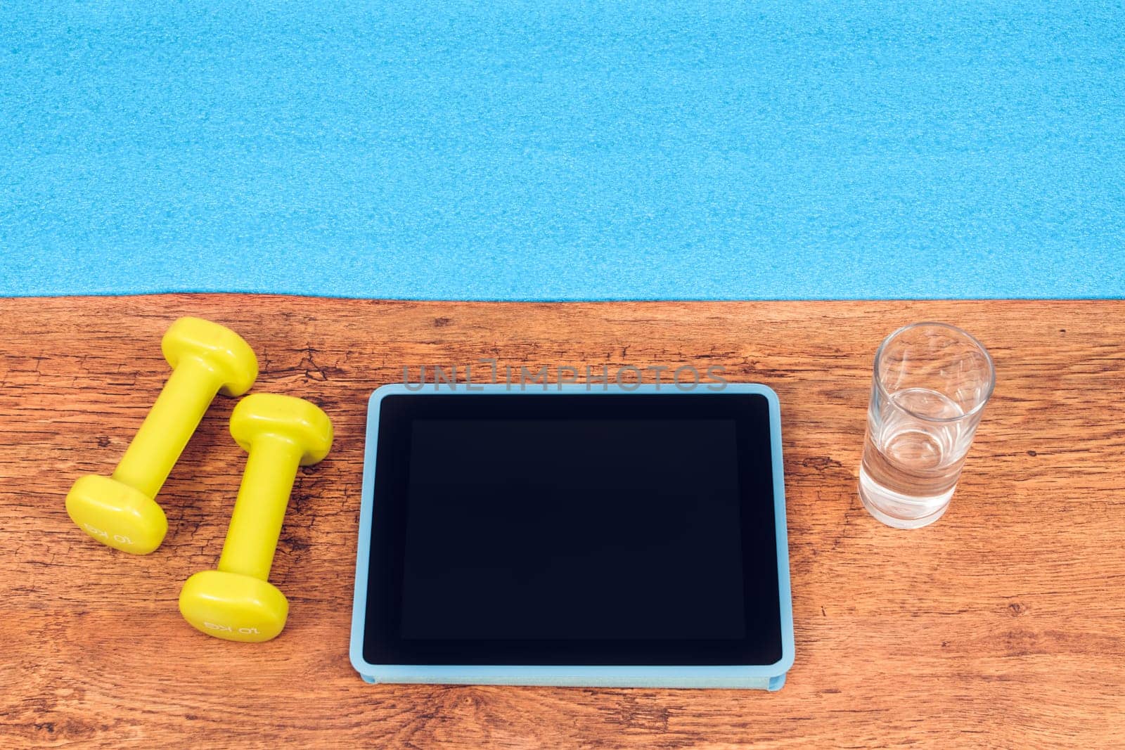 Tablet, dumbbells, glass of water prepared for workout with video fitness course