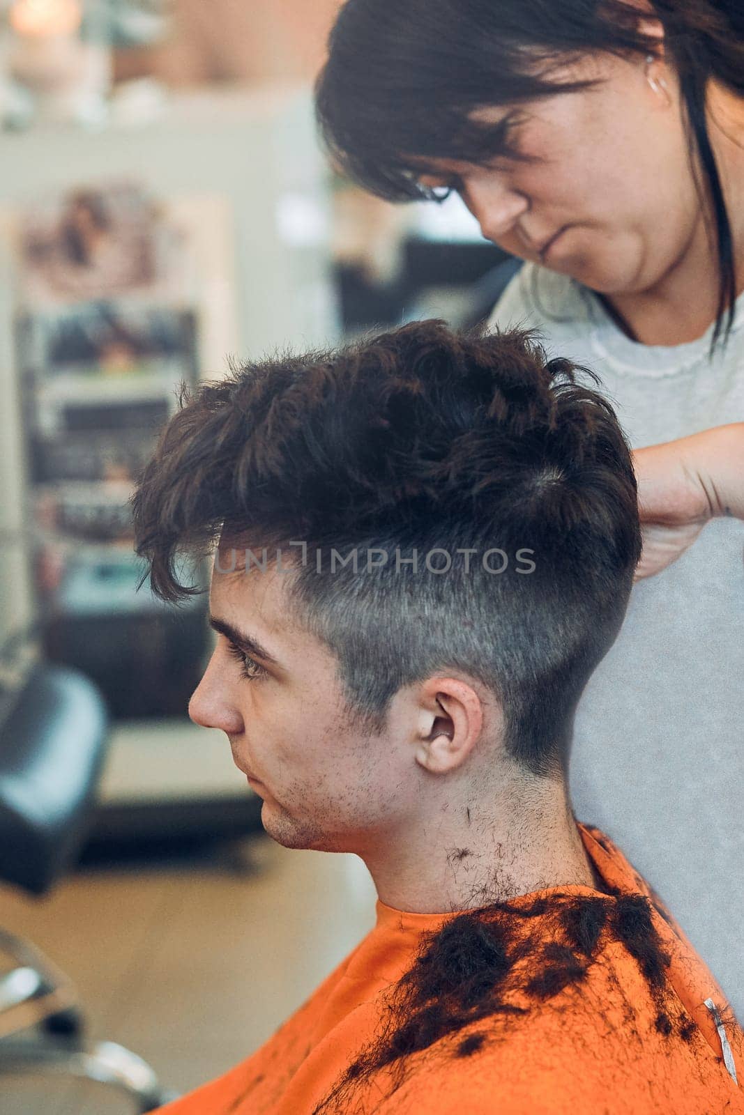 Hairdresser haircutting styling young man's hair in barbershop. Young woman working as a hairdresser in hair salon. Real people, authentic situations