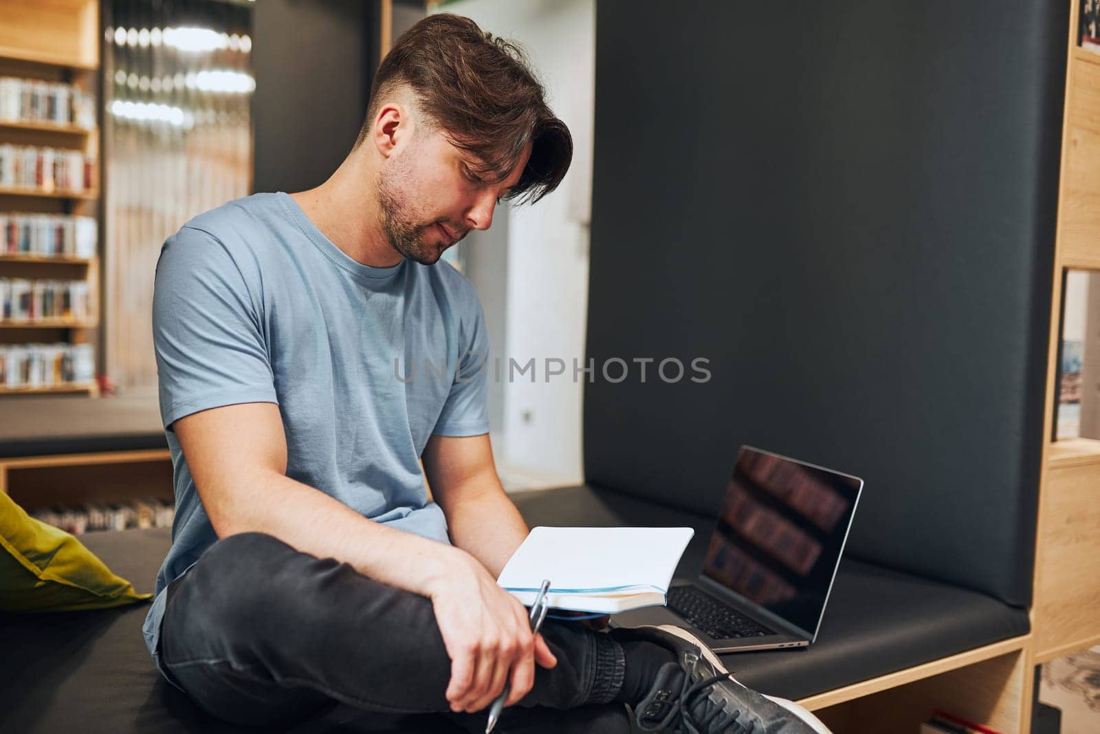 Student learning in university library. Young man reading his notes. Man using computer to learn. Focused student studying for college exams. Back to school