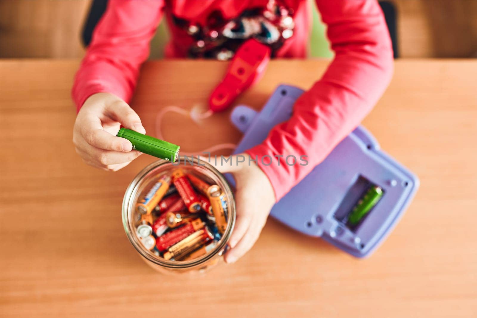 Little girl removing used batteries from toy and putting into jar for recycling. Child separating waste. Batteries only container