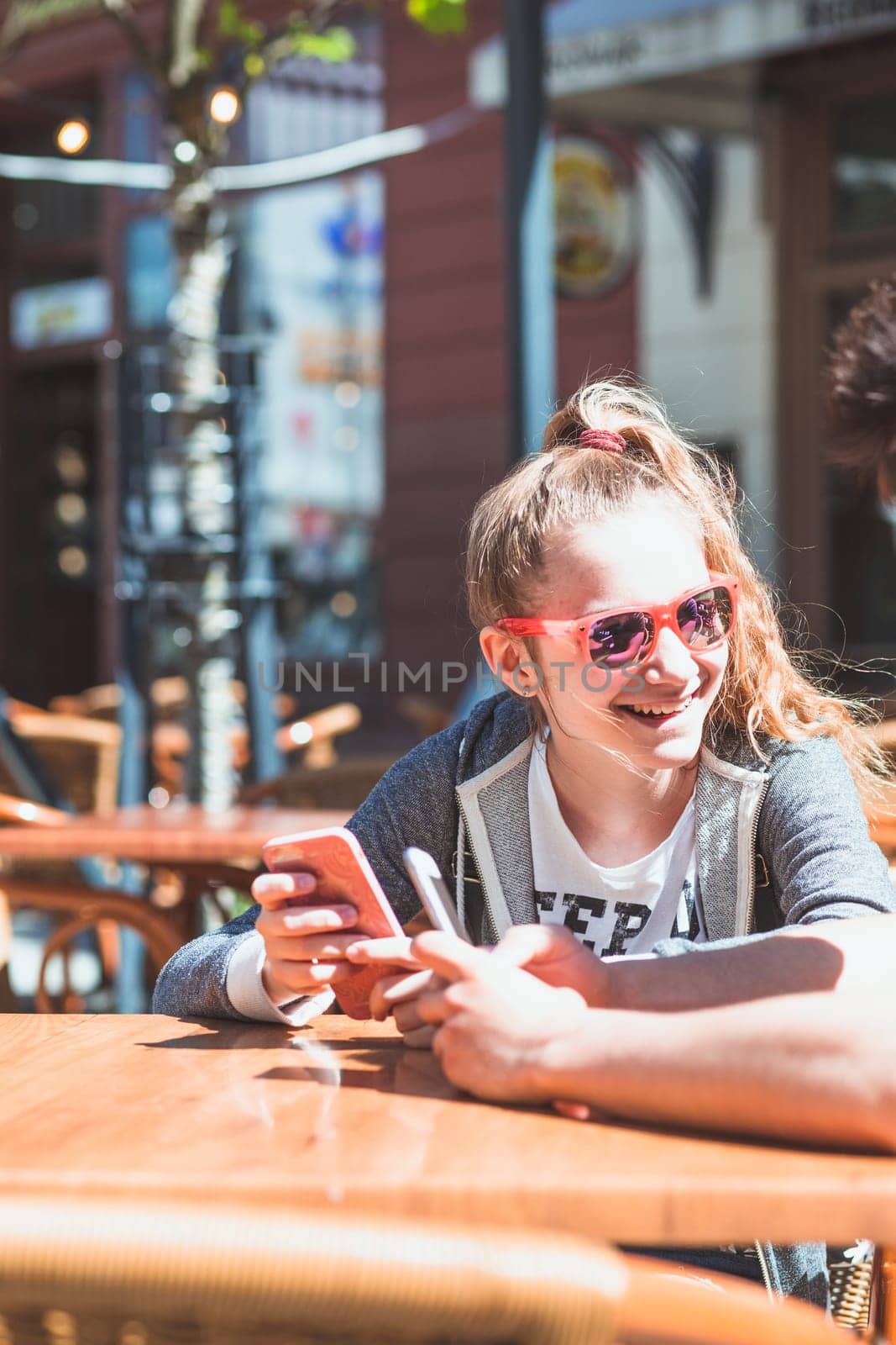 Young woman and man sitting in pavement cafe a the table talking and using mobile phones