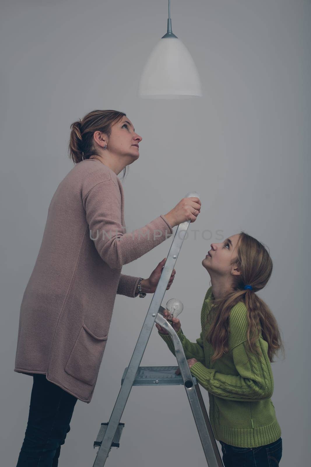 Woman and her daughter changing a light bulb together in dark room