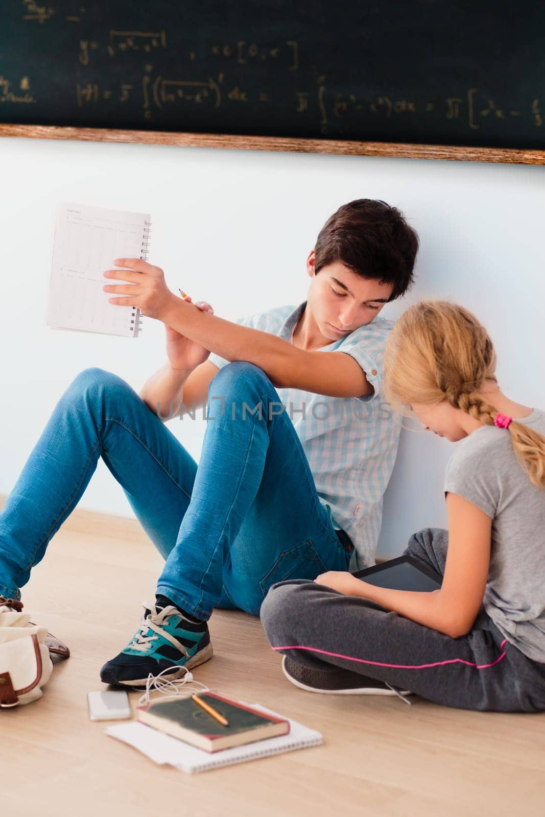 Teenagers learning in a classroom sitting by a blackboard on a floor