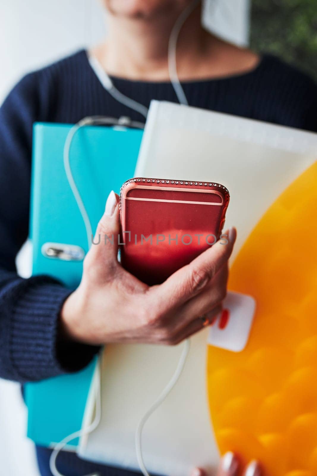 Woman working remotely doing job during call conversation on phone from home. Woman holding smartphone and documents in binder using headphones