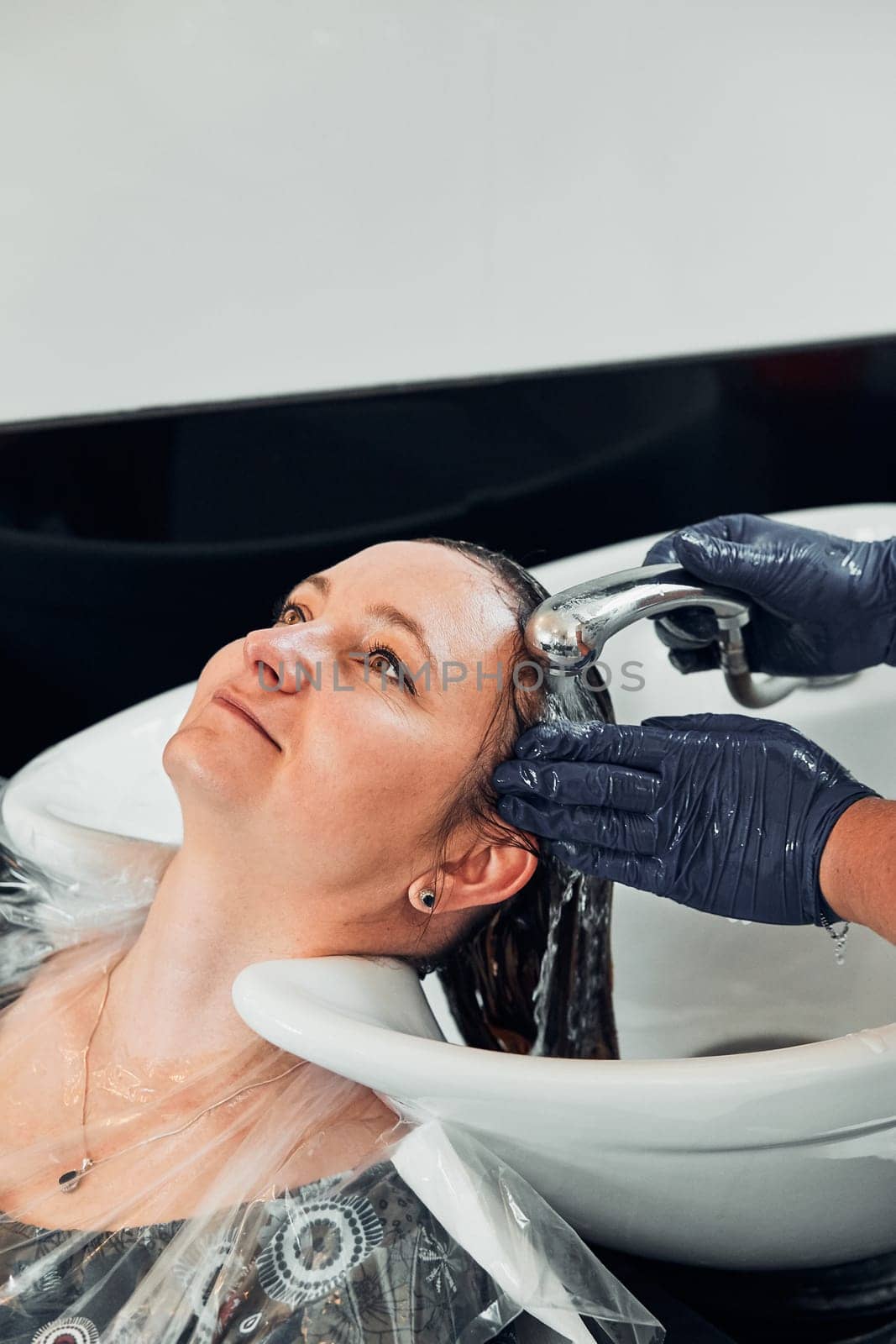 Hairdresser styling dyeing combing womans hair. Young woman working as a hairdresser in hair salon. Real people, authentic situations