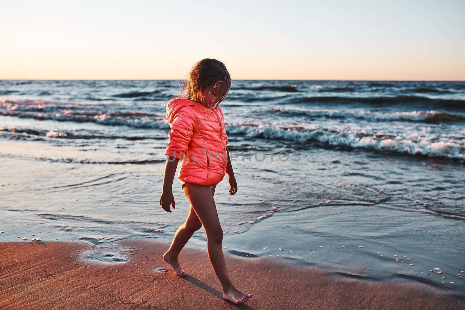 Little girl walking barefoot on a beach at sunset during summer vacation