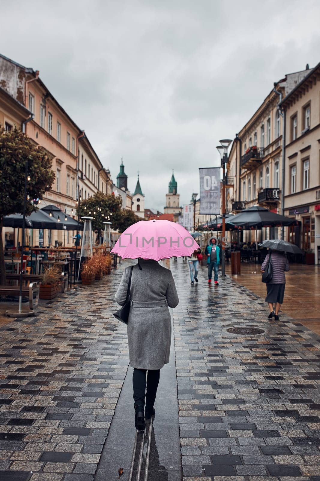 Back view of woman holding pink umbrella walking in a downtown on rainy gloomy autumn day