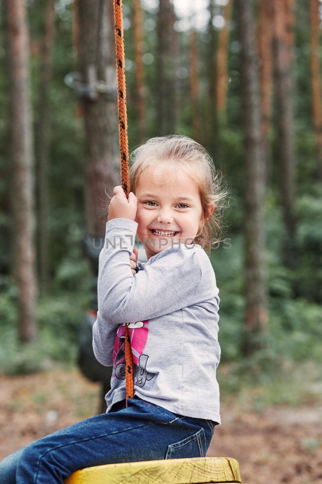 Happy girl riding on the zip line in rope park in forest while spending summer vacation. Real people, authentic situations