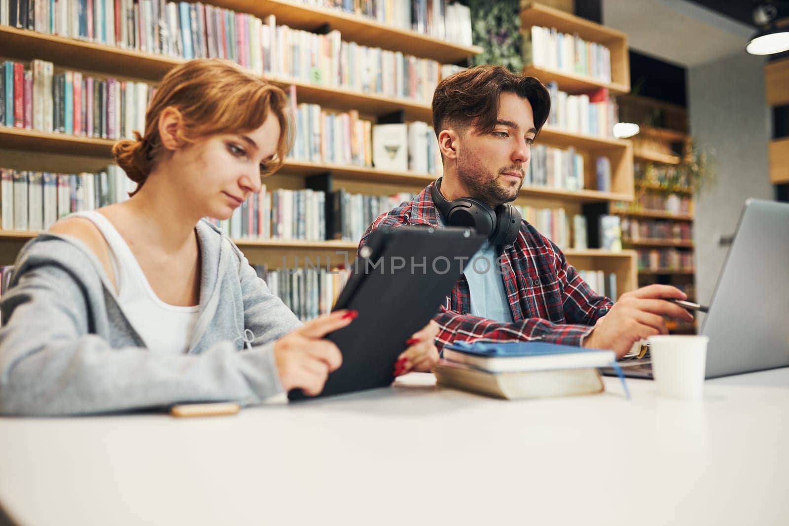 Students learning in university library. Young man preparing for test on laptop. Girl writing essay and making notes using computer. Focused students studying for college exams. Students discussing and learning together sitting at desk. Back to school