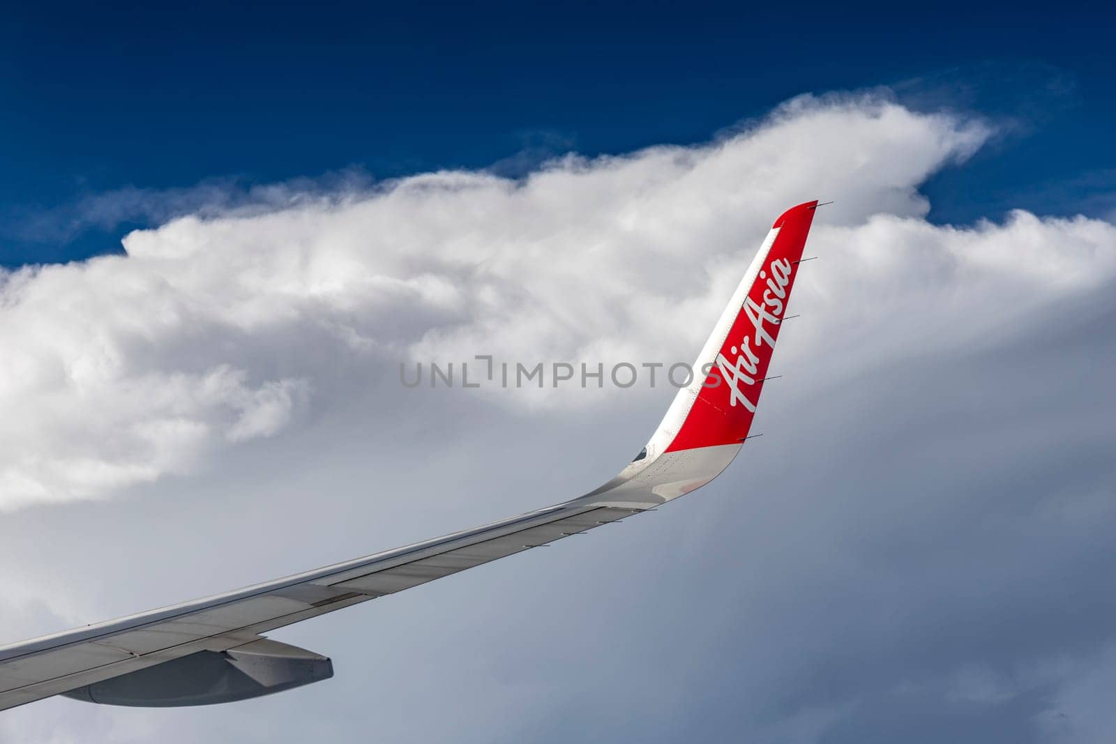 Bangkok Thailand - March 30, 2019: The trademark logo on the wing of AirAsia, a popular low-cost airline in many countries, is soaring in the sky against a backdrop of beautiful clouds.