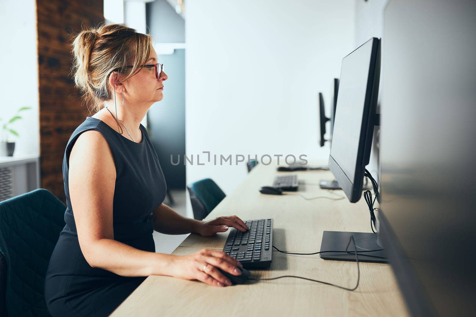Concerned businesswoman working on computer in office. Busy woman sitting at desk at front of computer monitor. Focusing on work. Open office. Copy space right