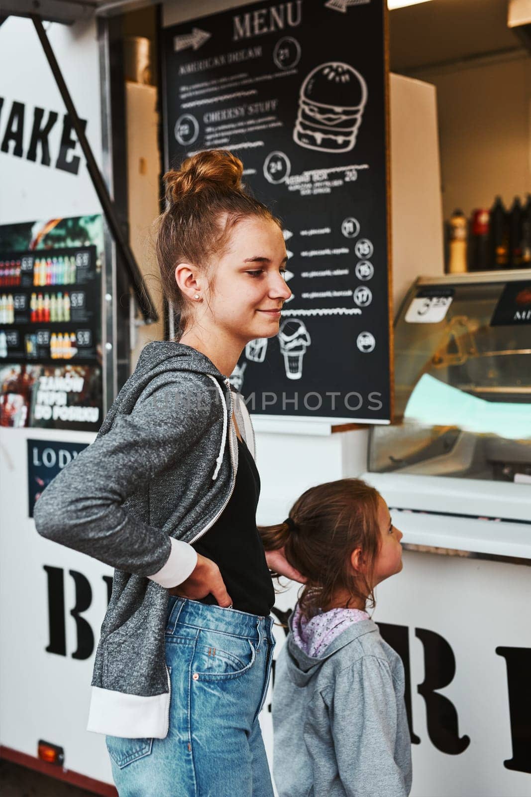 Teenage girl and her younger sister waiting for their order at front of a food truck during summer vacations