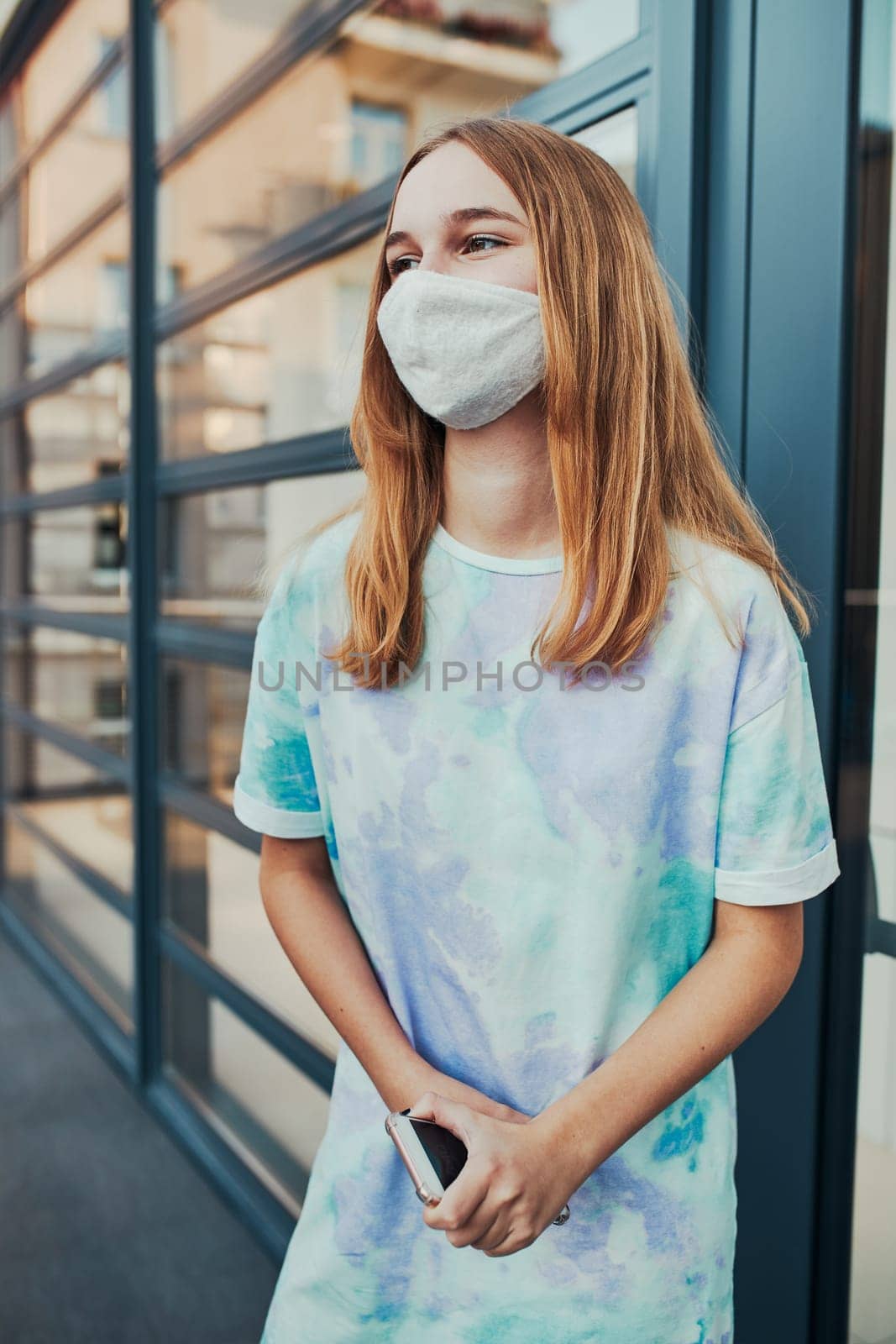 Portrait of young woman girl standing at store front downtown holding smartphone. Girl wearing face mask to avoid virus infection and to prevent the spread of disease in time of coronavirus