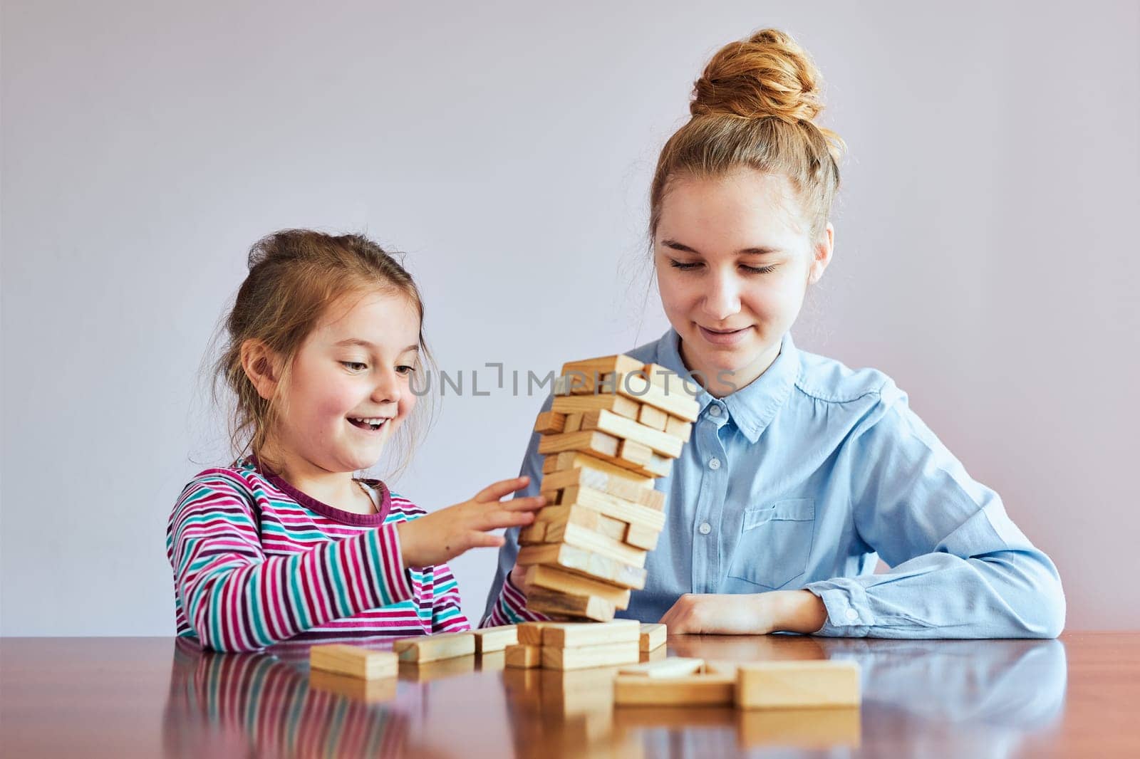 Little girl preschooler and her elder sister playing together with wooden blocks game toy. Siblings spending time sitting at desk at home