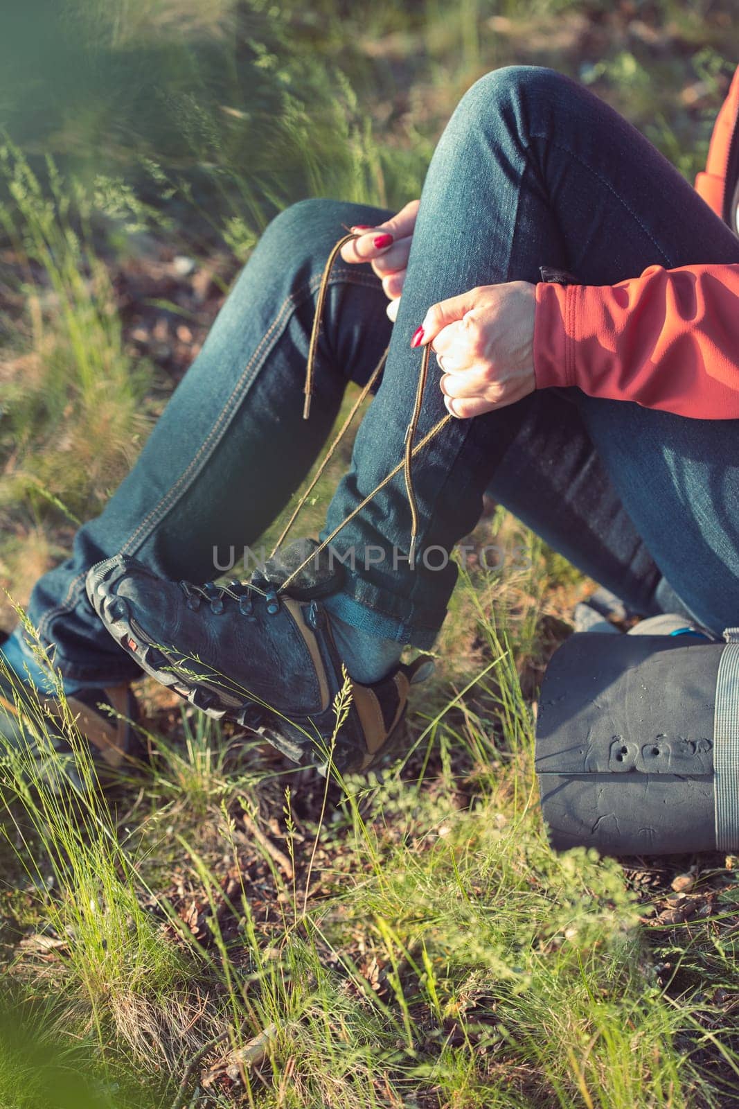 Young woman hiker with backpack lacing outdoor shoes during summer vacation trip in forest