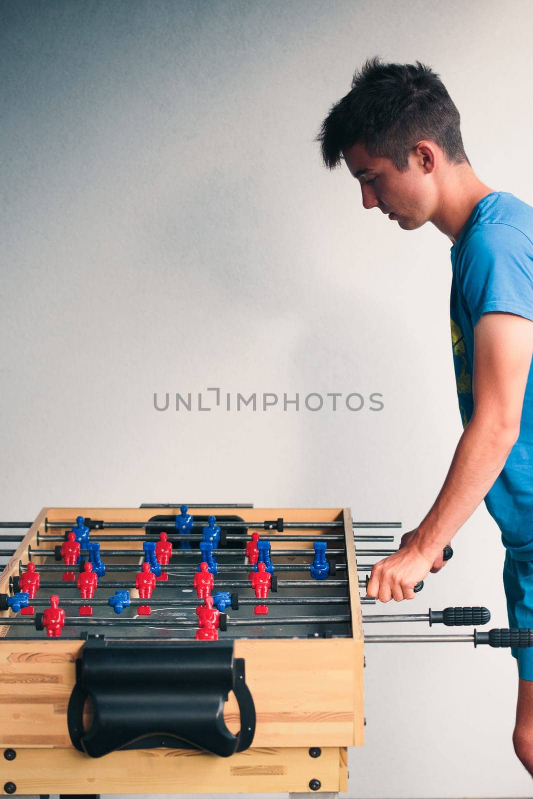 Young teenager boy playing table football with another player. Young people having fun, spending time together
