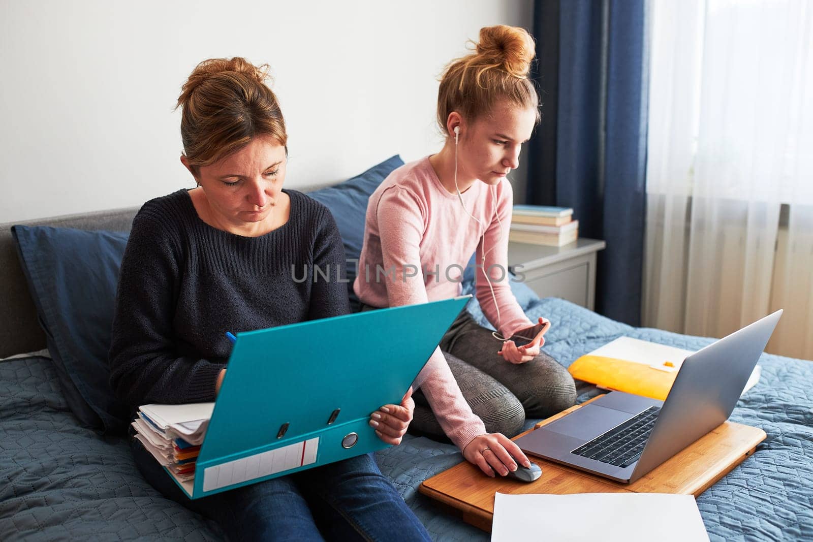 Women mother and daughter working learning remotely doing job during video chat call stream online course webinar lessons on laptop from home during COVID-19 quarantine. Women sitting on bed in front of computer looking at screen