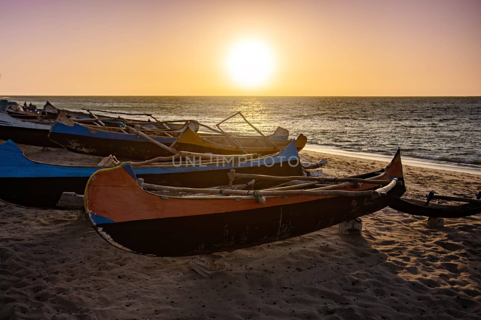 An empty wooden traditional fishing boat on the shore of Anakao beach, waiting for the next catch of the day in Madagascar. Sunset over sea on the tropical beach of Anakao, Toliara, Madagascar..