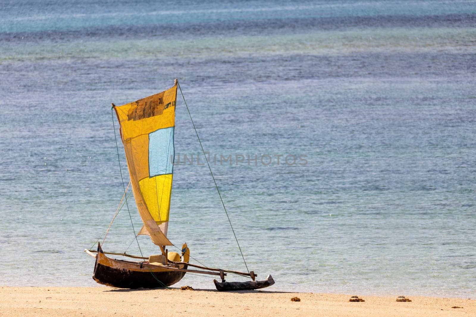 Tranquil scene of a wooden fishing boat resting on the golden sands of Nosy Ve Island's shoreline in Madagascar, with the clear blue water in the background. Nosy Ve, Anakao, Toliara, Madagascar