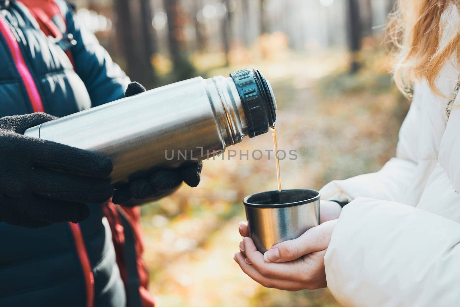 Women having break during autumn trip pouring a hot drink from thermos flask on autumn cold day. Active women wandering in a forest actively spending time