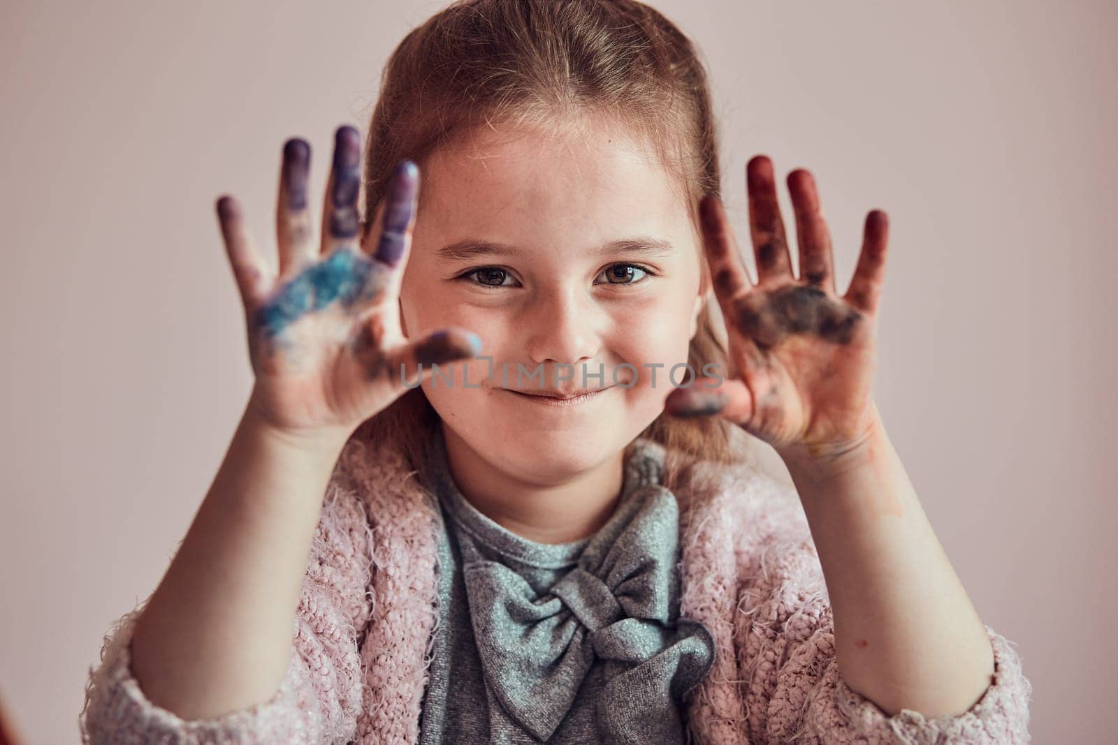 Little girl preschooler showing painted colourful hands. Child having fun making a stamps on sheet of paper with painted hands during an art class in the classroom