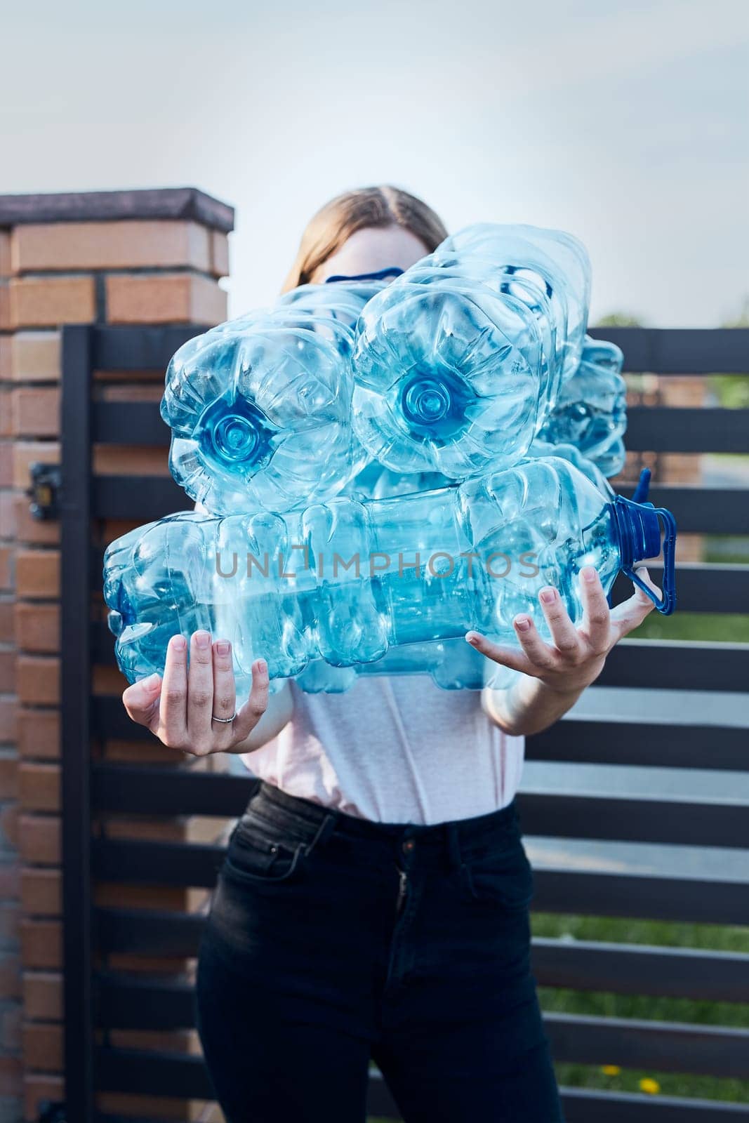 Young woman throwing out empty used plastic water bottles into trash bin. Collecting plastic waste to recycling. Concept of plastic pollution and too many plastic waste. Environmental issue