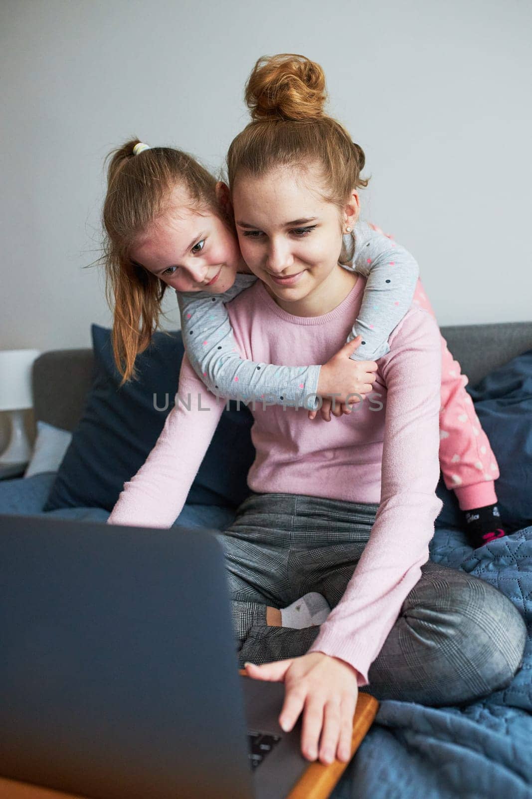 Grandchildren teenage girl and her younger sister talking on video call with granparents on laptop from home during COVID-19 quarantine. Girls sitting on bed in front of computer