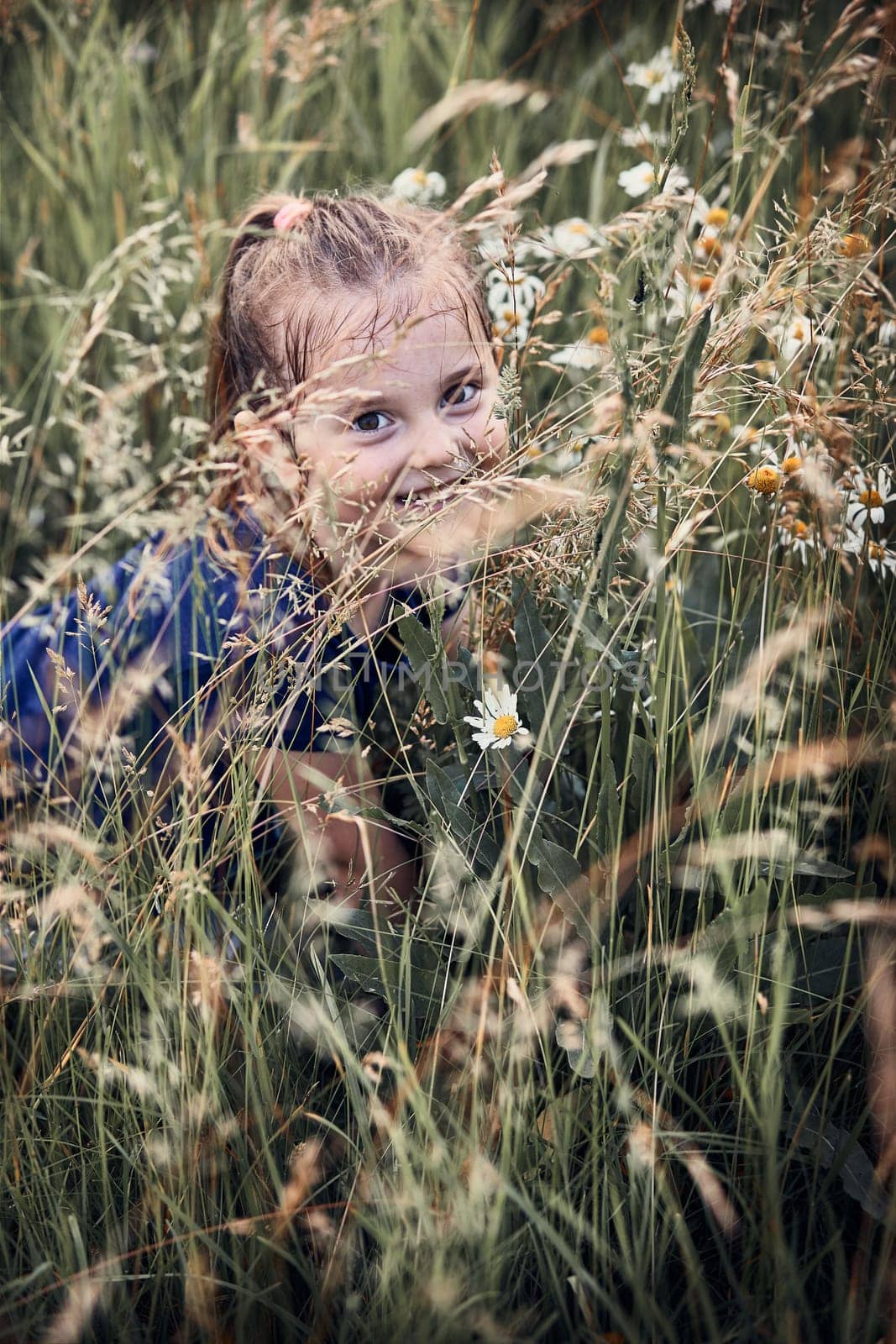 Little happy girl playing in a tall grass in the countryside. Candid people, real moments, authentic situations