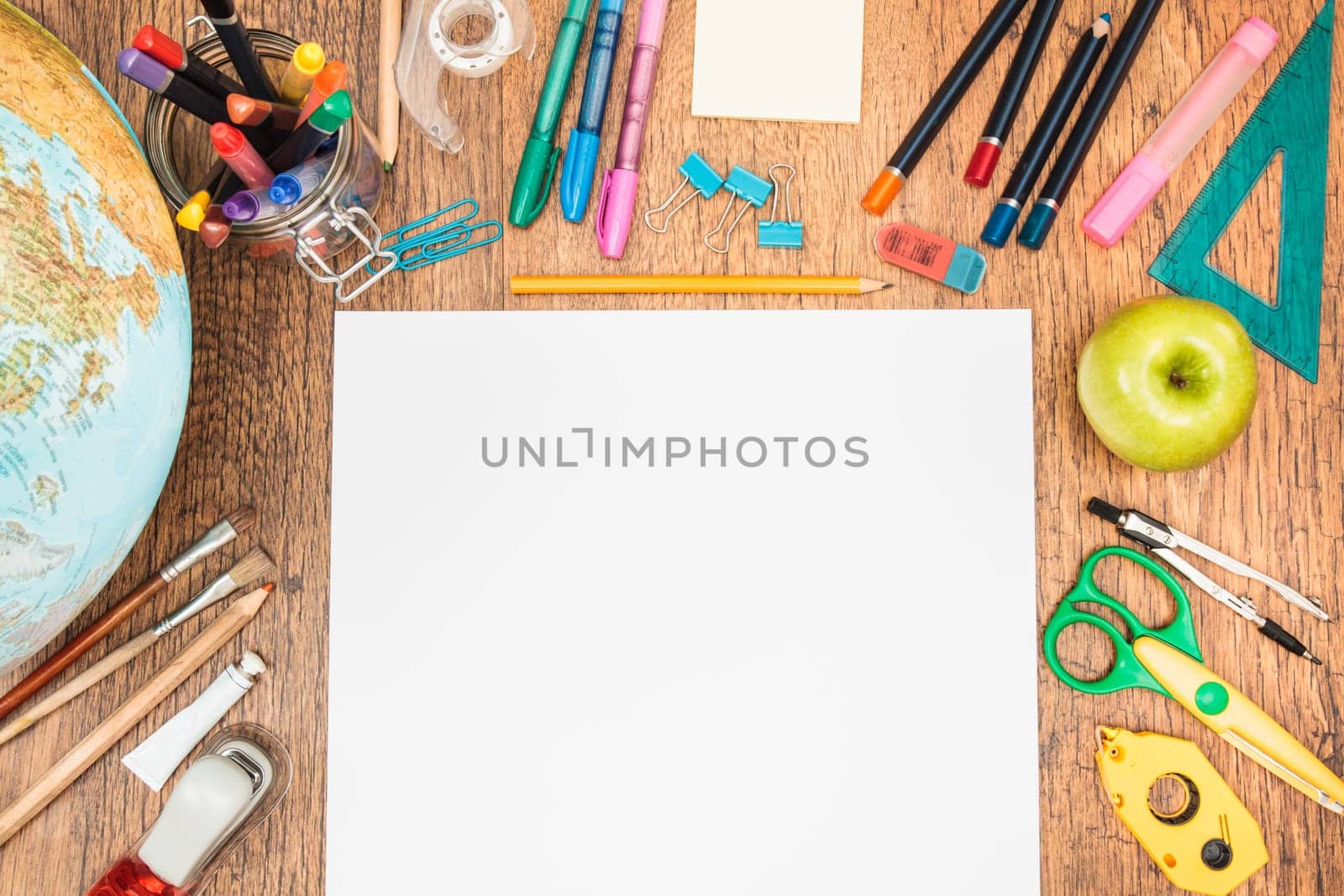 School accessories, pencil, pen, scissors, blank sheet of paper on a wooden desk. View from above