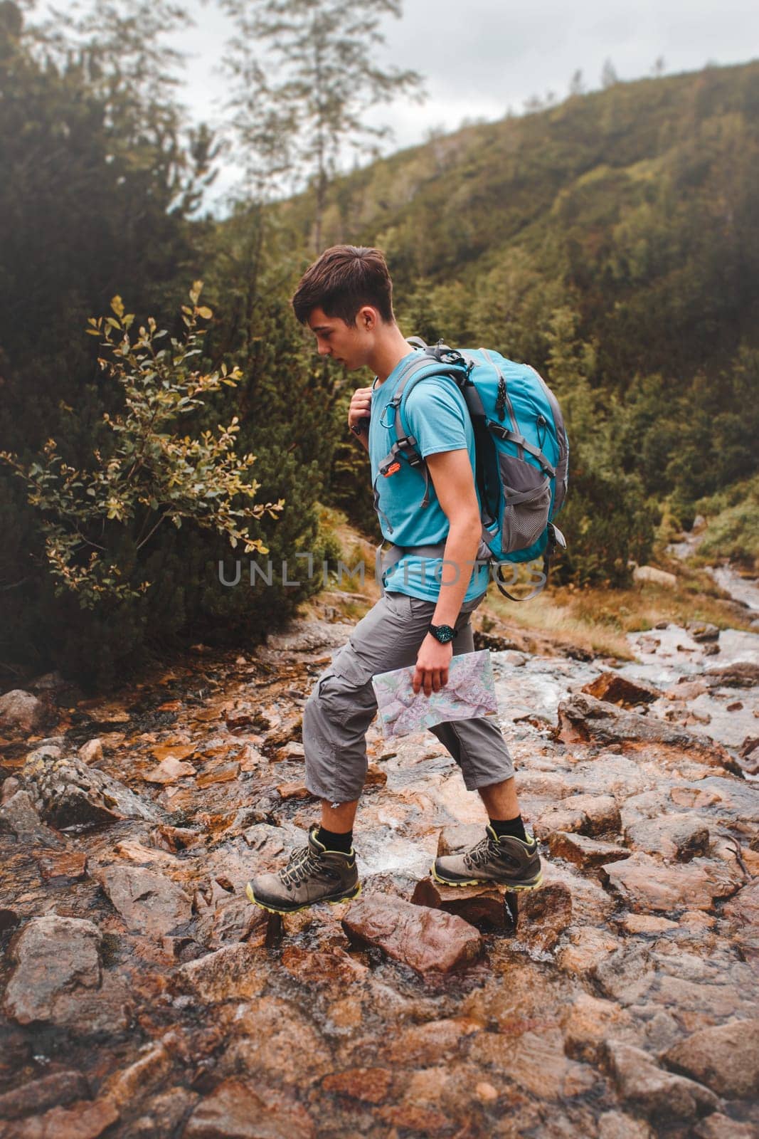 Boy with backpack going across a mountain stream during hiking in mountains